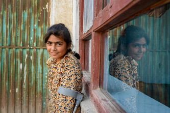 Marwa steht lächelnd vor dem Fenster einer Hauswand und stützt sich auf einer Gehhilfe ab.