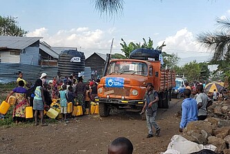 Etwa 20 Menschen stehen vor einem Laster mit Trinkwasser.