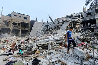 Ein Jugendlicher steht auf den Trümmern eines völlig zerstörten Mehrfamilienhauses