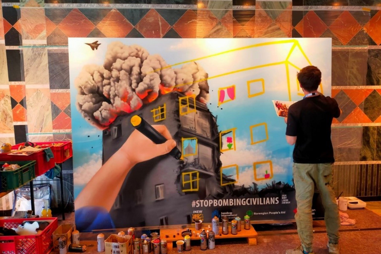 Das Graffiti vom Konferenztag, an dem einer der Künstler gerade arbeitet. Das Kunstwerk zeigt ein von Bomben zerstörtes Haus. Der zerstörte Teil des Hauses wird von einer Kinderzeichnung wieder „aufgebaut“. / © HI