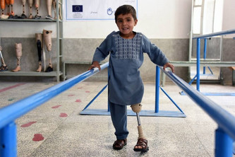 Sanaullah, ein Junge in hellblauen Kleidern ist in dem HI Reha-Zentrum zu sehen. Unter seinem langen Oberteil ist die Beinprothese deutlich zu sehen. Hier ist er bei Laufübungen abgebildet