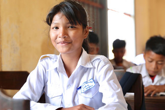 Srey Neang sitzt in einem Klassenzimmer und lächelt in die Kamera.